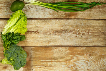Green vegetables, broccoli, avocado, onions, spinach on the edge of a table of rough boards.