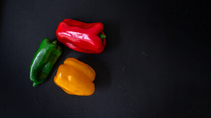 Three coloured peppers on a dark surface