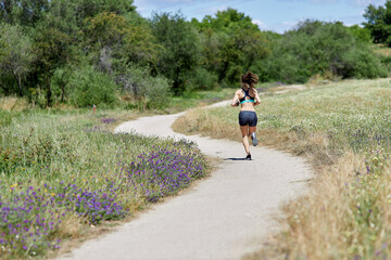 Back view of slim attractive woman running around the field. Unrecognizable person