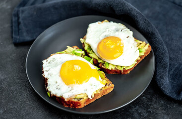 Toasts with avocado and fried eggs on a cutting board on a stone background
