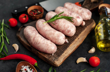Raw chicken sausages with spices on a cutting board on a stone background