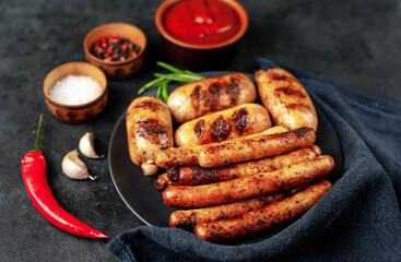 Various grilled sausages with spices on a black plate on a stone background