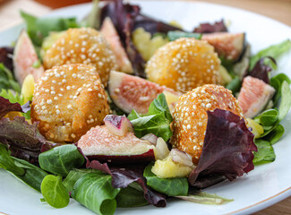 Fancy salad with goat cheese balls, figs and mango over a wooden table. 