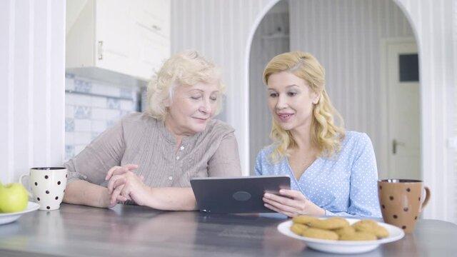 Senior mother and daughter shopping online, discussing photos on tablet, fun
