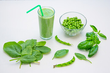 Smoothie in a glass and ingredients – green peas, basil and spinach leaves on a white background. Healthy vegan cocktail. 