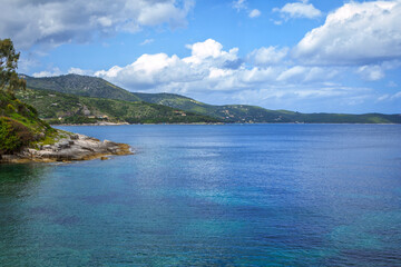 Beautiful landscape - sea lagoon with turquoise water, stones and rocks, blue sky with clouds and mountains on the horizon. Corfu Island, Greece.
