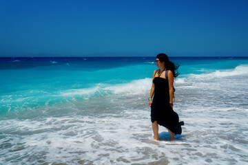 Sea wave washes legs of Happy woman traveler, the wind plays in her hair