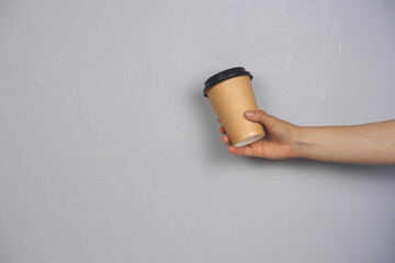 female hand holding coffee to go blank cup against concrete gray wall copy space