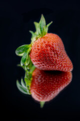 A single strawberry on a black mirror.