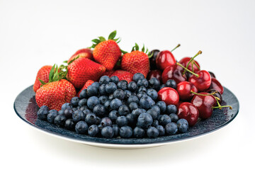 A blue patterned plate with blueberries, strawberries, and cherries on a white background.