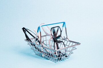Fototapeta na wymiar a few glasses in a toy metal shopping basket on a light blue background, glasses for adults and children, buying glasses in an optics store