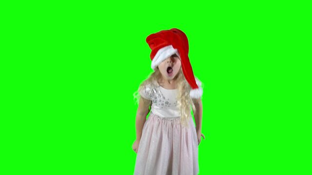 Tiny girl puts on a Christmas hat and playing naughty. green background.