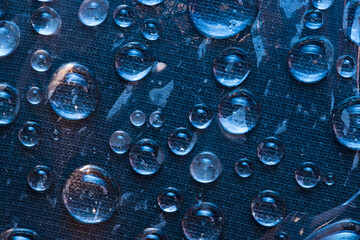 Texture. Transparent raindrops are located on the blue cloth background. Close-up. 
