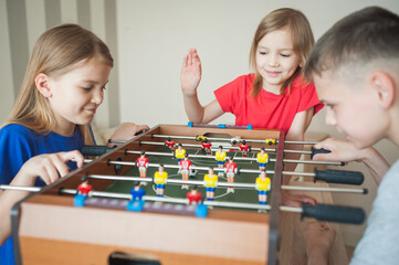 Children play table football in a children's room, two girls and a boy
