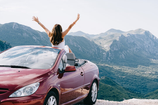 Happy Woman Sits In A Red Convertible Car With A Beautiful View