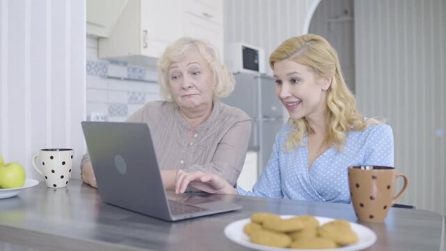 Glad mother and daughter choosing clothes online, using shopping app on laptop