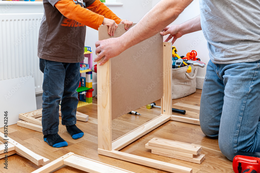 Wall mural Father and son assembling flat pack furniture. A set of two small chairs with desk in boys bedroom.