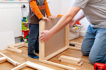 Father and son assembling flat pack furniture. A set of two small chairs with desk in boys bedroom.