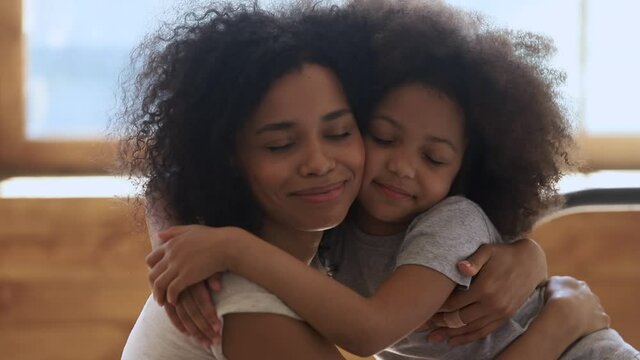 Loving affectionate african american family mom and cute little child daughter embracing bonding together, happy mother foster parent hugging small kid girl cuddling enjoying tender moment connection
