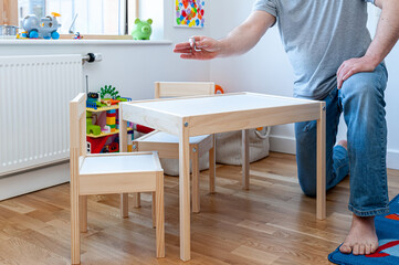 A parent assembling flom flat pack a set of two small chairs with desk in childs bedroom.