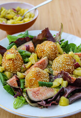Fancy salad with goat cheese balls, figs and mango over a wooden table. 