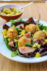 Fancy salad with goat cheese balls, figs and mango over a wooden table. 