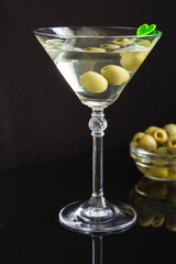 Martini cocktail with green olives in a glass on a black  background. Closeup. Location vertical.