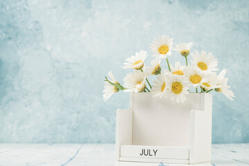 White cube calendar for july decorated with daisy flowers on table with copy space - obrazy, fototapety, plakaty