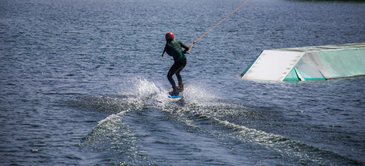 The man does wakeboarding on the water in the summer in a helmet and wetsuit.