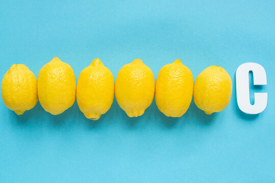 top view of ripe yellow lemons and letter C on blue background