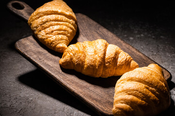 fresh baked croissants on wooden cutting board on concrete grey surface in dark