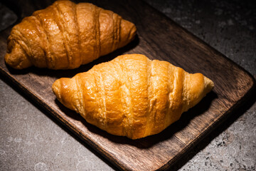 fresh baked croissants on wooden cutting board on concrete grey surface in dark