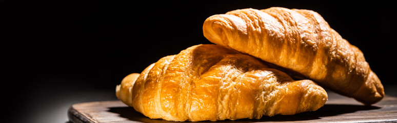 fresh baked croissants on wooden cutting board isolated on black, panoramic shot