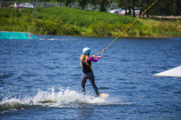 The man does wakeboarding on the water in the summer in a helmet and wetsuit.
