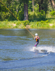 The man does wakeboarding on the water in the summer in a helmet and wetsuit.