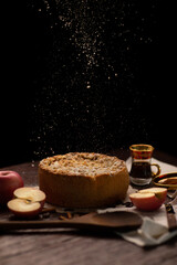Sprinkling sugar powder from above on homemade apple pie with ingredients on rustic dark background. Classic autumn Thanksgiving dessert - organic apple pie.