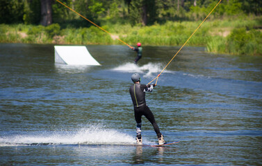 The man does wakeboarding on the water in the summer in a helmet and wetsuit.