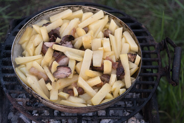 jacket potatoes, squash and sausages are cooked in a large frying pan on an open fire