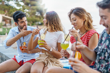Group of trendy happy young people talking and having fun drinking tropical cocktails together...