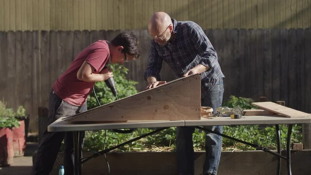 A father and his teenage son build a wooden ramp in the backyard