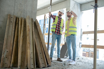 Building workers in yellow vests and gloves standing near pile of boards, discussing what to do with them