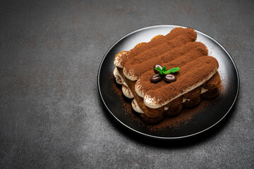 Classic tiramisu dessert on ceramic plate on dark concrete background