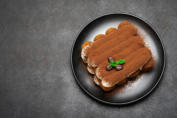 Classic tiramisu dessert on ceramic plate on dark concrete background