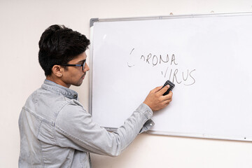 A young boy in denims erasing corona virus written on a white board, representing that corona virus will be gone soon.