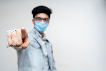 A young boy wearing a protection mask on his face pointing a finger towards the camera, selective focus.