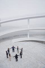 Business people holding hands standing in circle in modern courtyard