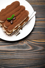 Classic tiramisu dessert on ceramic plate on wooden background