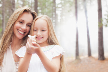 Smiling mother and daughter holding butterfly in woods