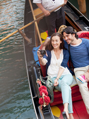 Fototapeta na wymiar Smiling couple taking photographs in gondola on canal in Venice
