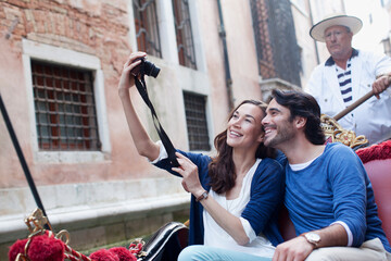 Smiling couple taking self-portrait digital camera in gondola on canal in Venice © Sam Edwards/KOTO